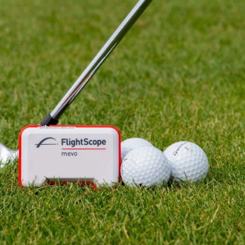 FlightScope Mevo golf launch monitor with two golf balls on a golf course green, used for golf swing analysis and practice, perfect for golf simulator setups and improving golf game performance.