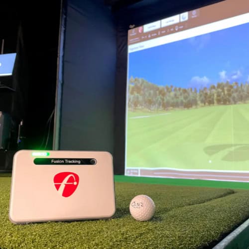 High-tech golf simulator with launch monitor, golf ball, and large screen displaying virtual golf course for realistic practice and play.