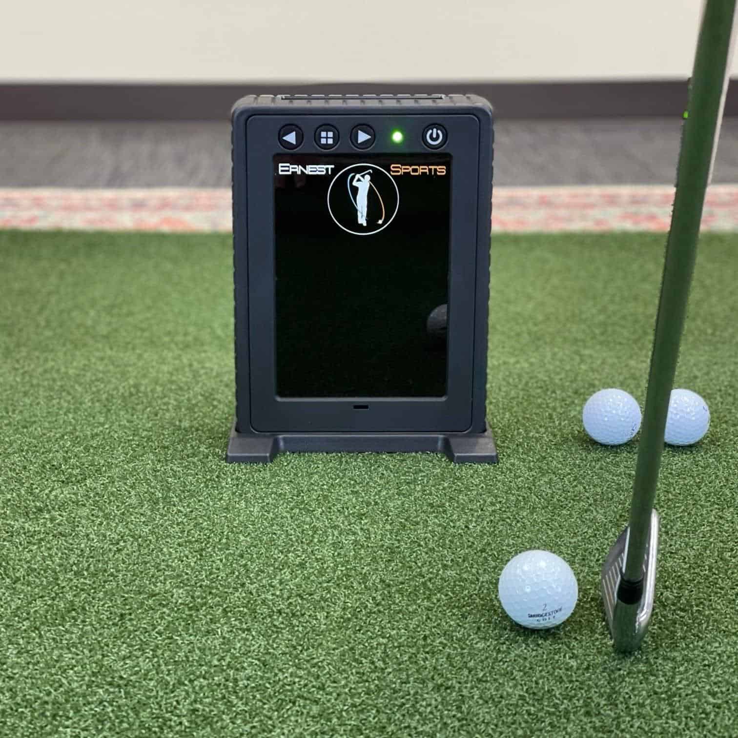Golf simulator launch monitor device with screen and golf balls on artificial turf for indoor golf practice.