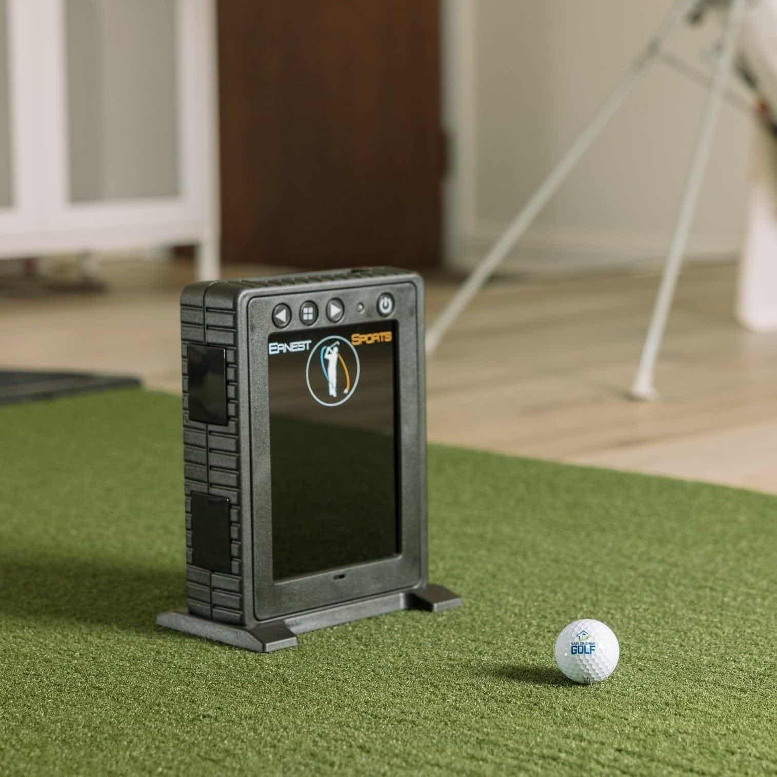 Golf simulator launch monitor device with screen and sensors on artificial turf for indoor golf practice.