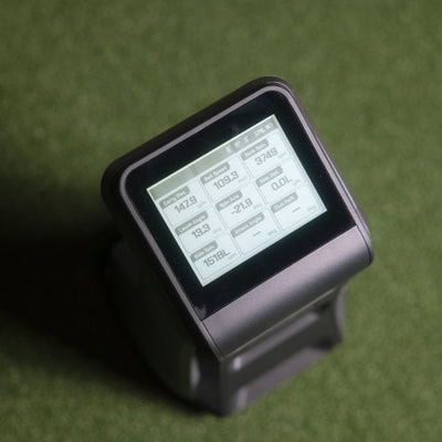Close-up of a golf launch monitor device displaying swing data on a digital screen, used for improving golf performance and shot analysis.